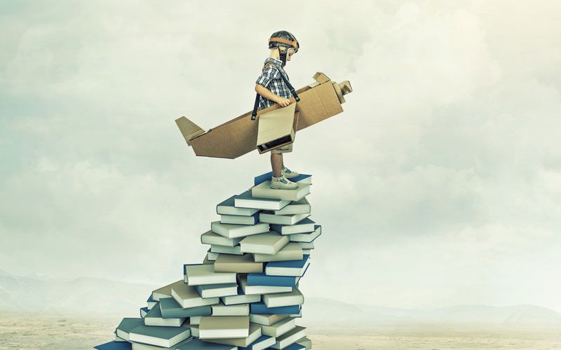 enfant avec un avion en carton en haut de la pile de livres